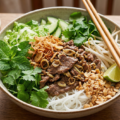 Un grand bol de Bo Bun traditionnel vietnamien avec bœuf sauté, vermicelles, herbes fraîches et cacahuètes, prêt à être dégusté.